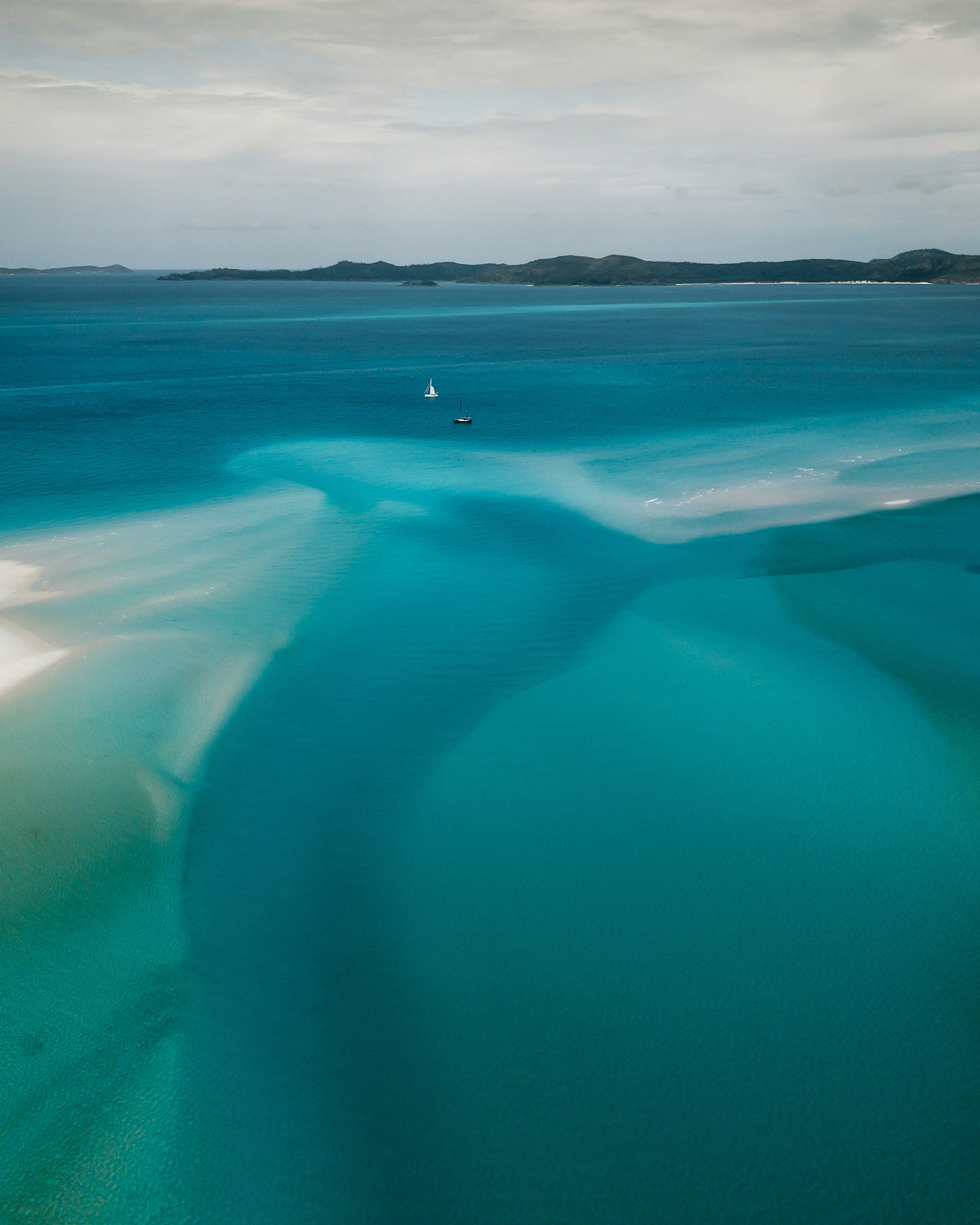 an aerial view of a body of water with a sailboat in the distance
