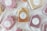 Several handmade soaps, each wrapped in paper and labeled 'Eden Crafted,' are arranged on a light fabric background. The soaps are in different colors, including shades of pink, beige, and brown. Each soap bar carries a round label with a simple botanical design and text indicating they are 100% handcrafted and locally made.