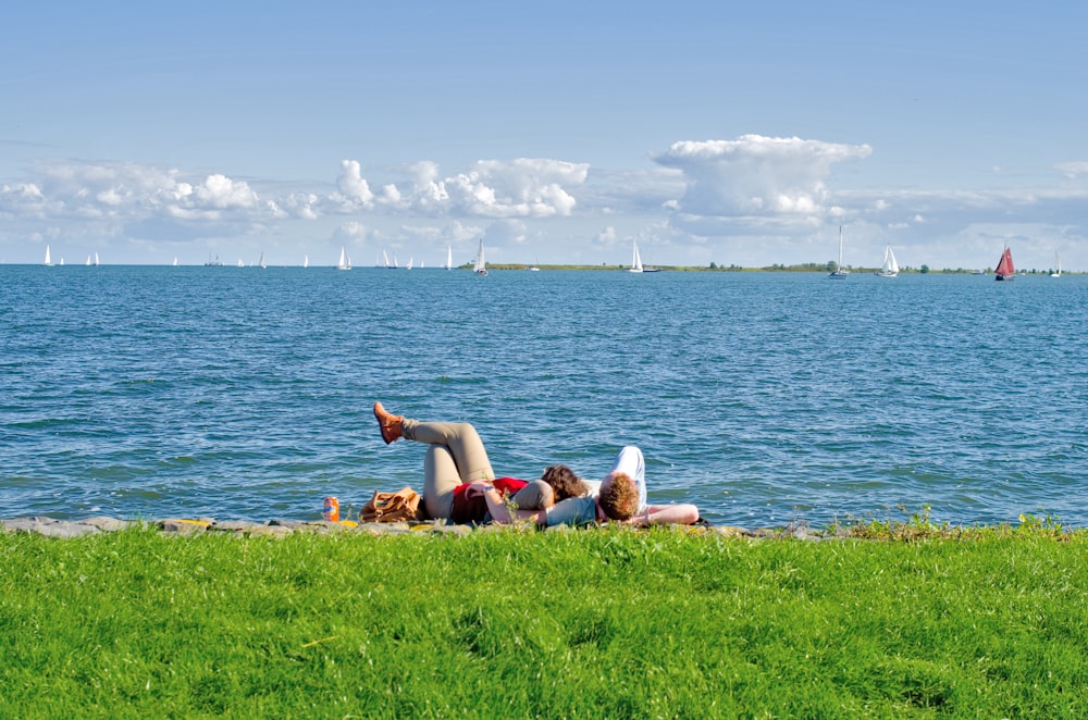 낮 동안 수역 근처의 푸른 잔디밭에 누워있는 2 명의 여성