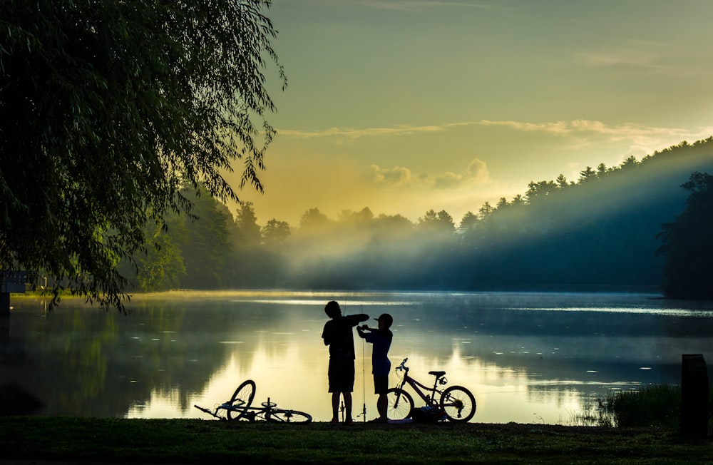 silhouette of 2 people riding bicycle on lake during sunset