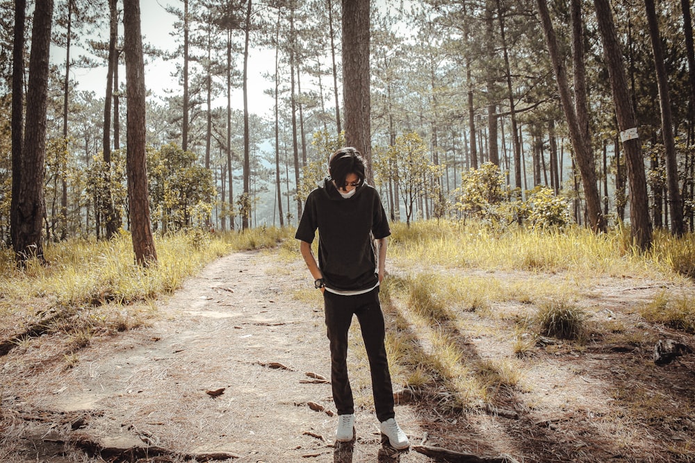 man in black long sleeve shirt and black pants standing on dirt road surrounded by trees