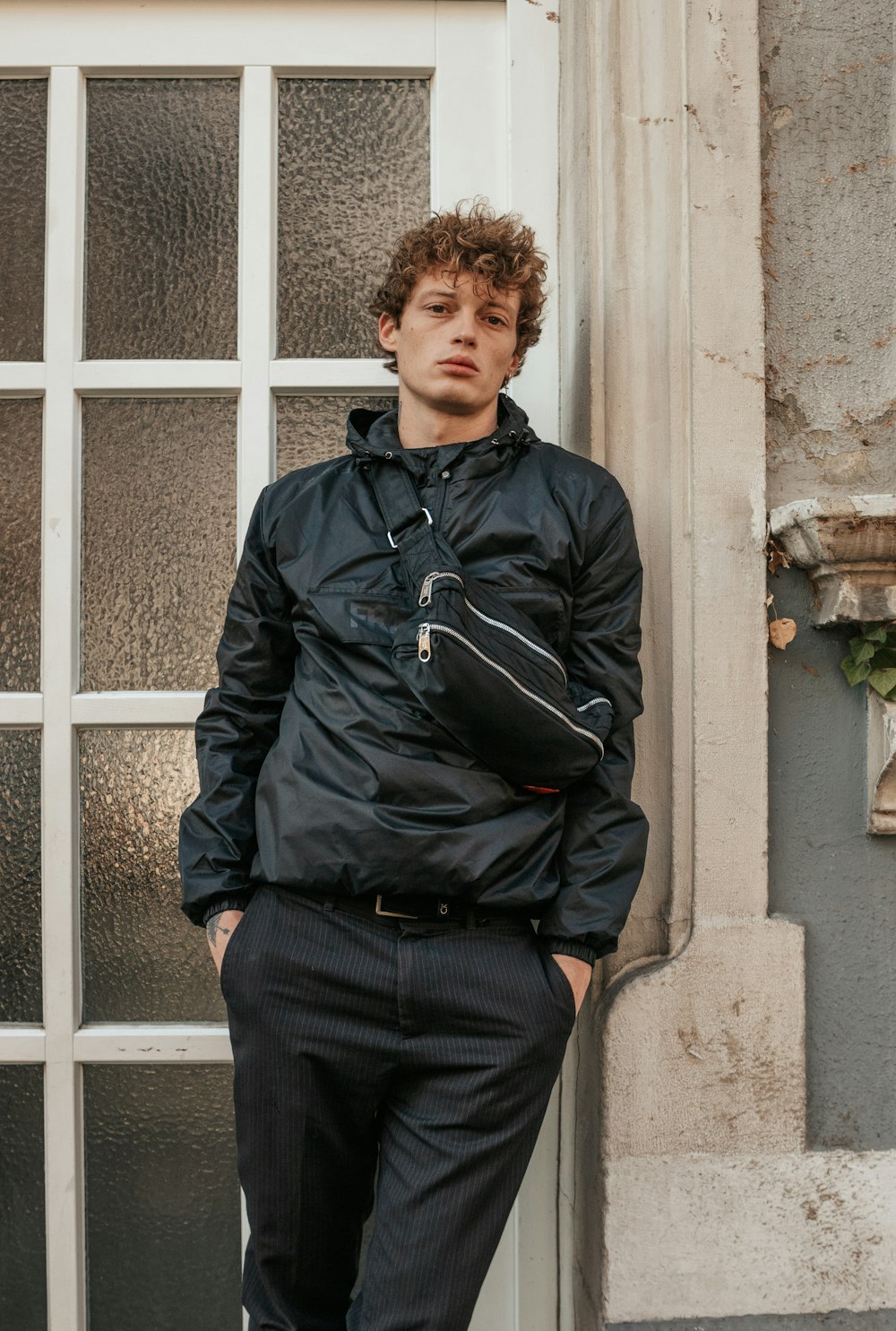 man in black leather jacket and black pants standing beside white wooden window