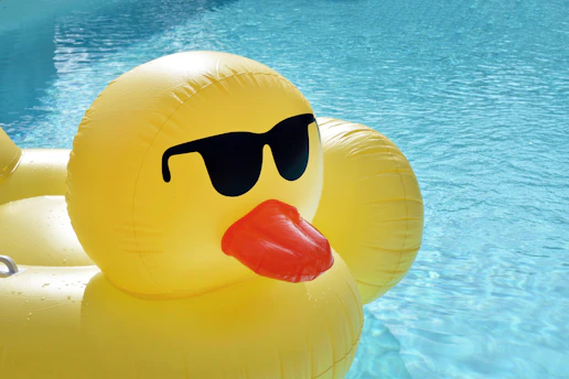 A yellow inflatable duck with black sunglasses floating in a blue swimming pool