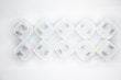 Nine white electrical plug adapters are arranged in a diamond pattern on a white background. Each adapter has two flat prongs, and some have small circular markings in green or pink.
