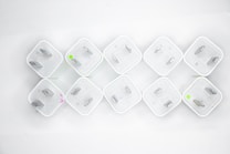 Nine white electrical plug adapters are arranged in a diamond pattern on a white background. Each adapter has two flat prongs, and some have small circular markings in green or pink.