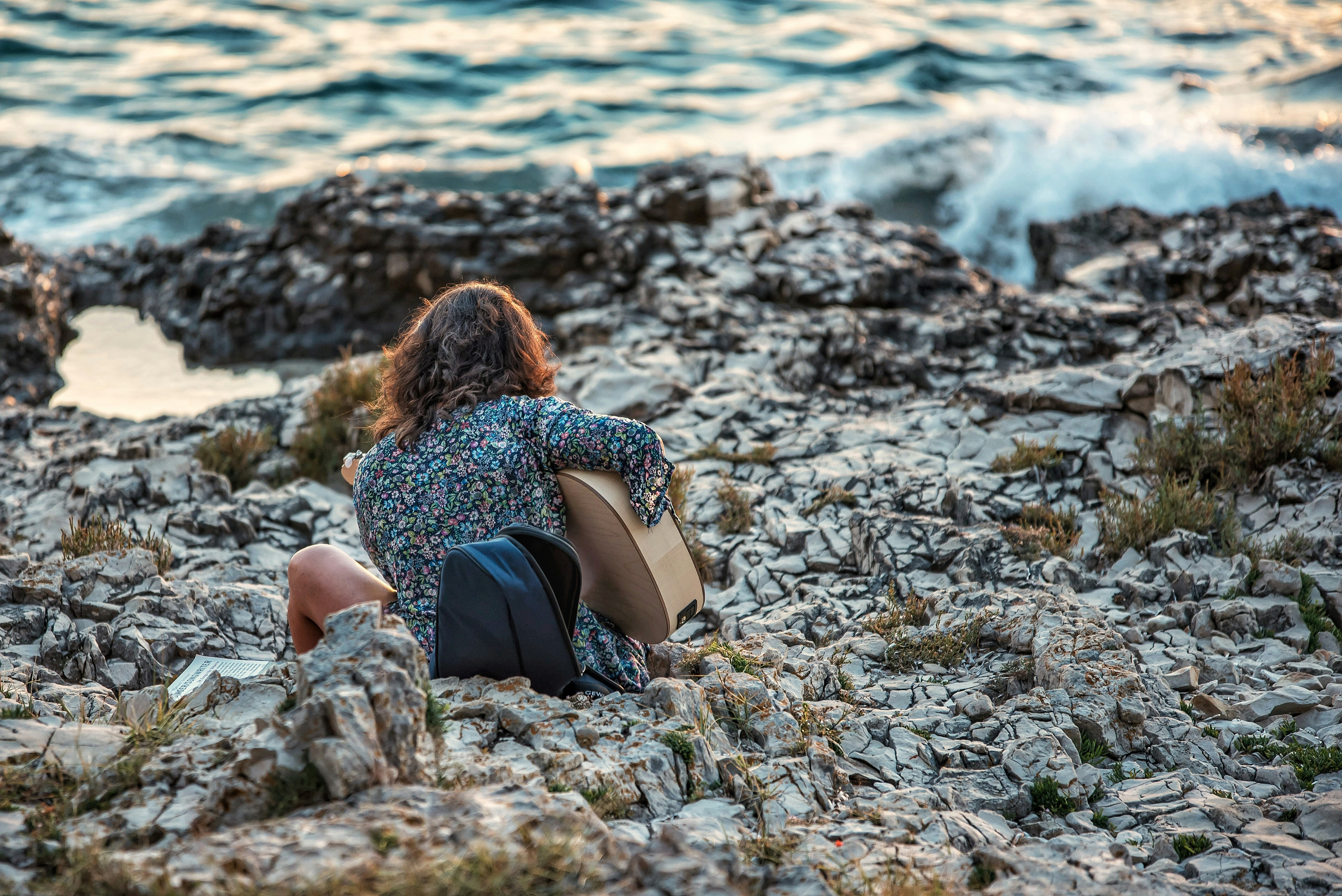woman in black and white polka dot dress sitting on rocky shore during daytime