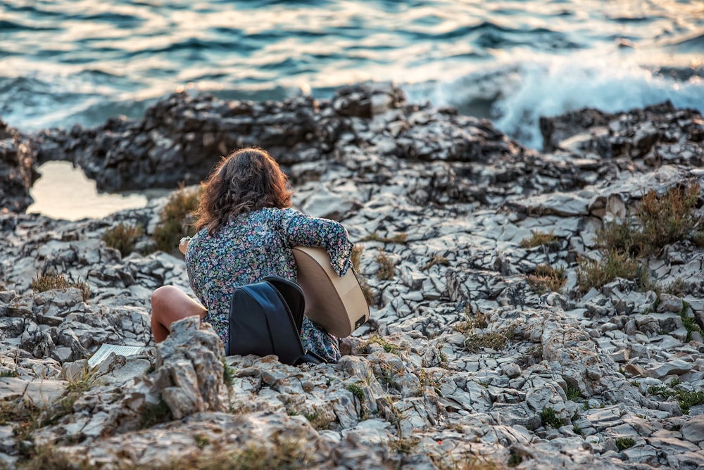 woman in black and white polka dot dress sitting on rocky shore during daytime