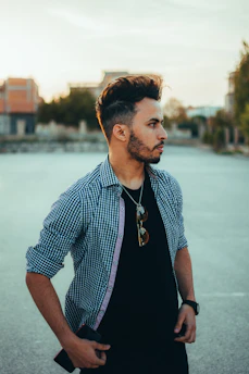 A stylish man with well-groomed hair and beard enjoying a sunny day outdoors.