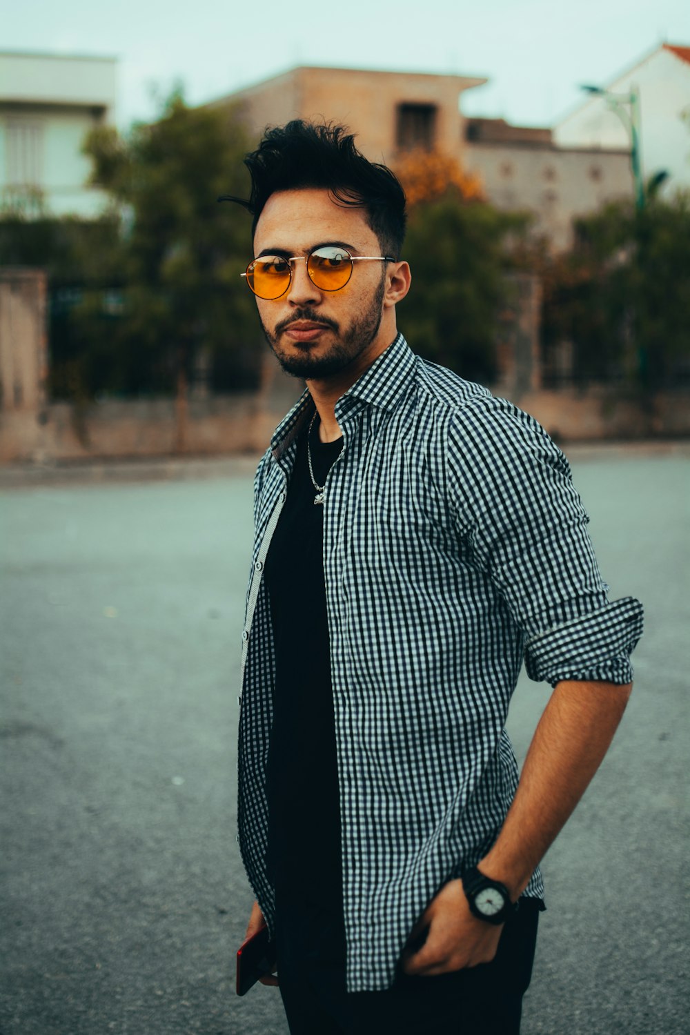 man in black and white checkered button up shirt wearing black sunglasses standing on gray concrete