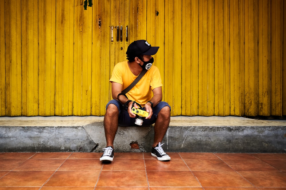 man in yellow t-shirt and black shorts sitting on floor