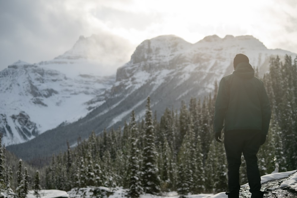 man in green jacket standing on snow covered ground near green pine trees during daytime