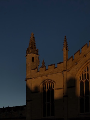 A Gothic-style building is partially illuminated against a dark twilight sky, with intricate spires and arched windows highlighted by warm light.