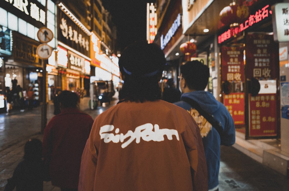 man in brown and white hoodie standing in front of people walking on street during nighttime