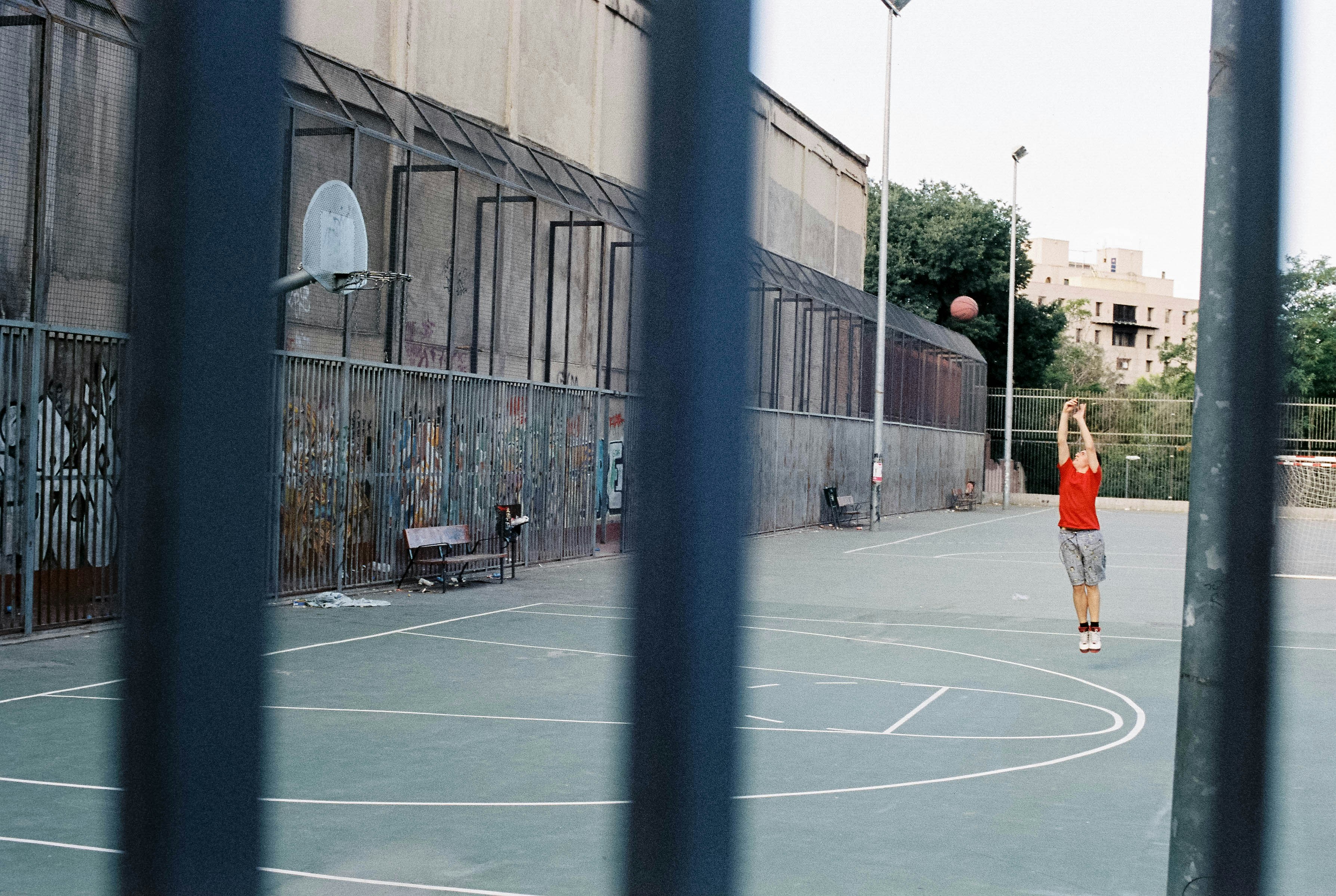 man in orange shirt and black shorts walking on basketball court during daytime basketball court teams background