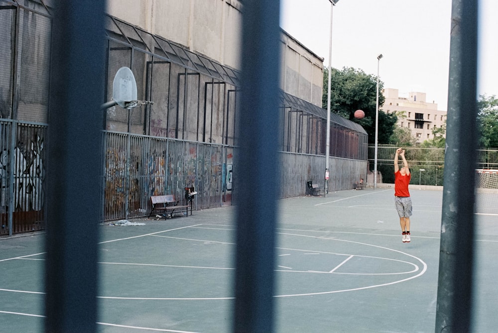 man in orange shirt and black shorts walking on basketball court during daytime