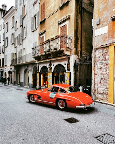 A classic red coupe with clean lines parked on a cobblestone road