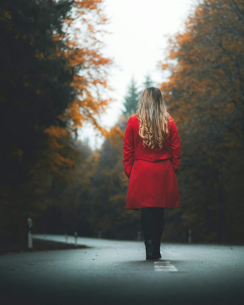 woman in red coat standing on road during daytime