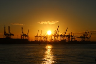 Sunset view over the port of Candeias with silhouettes of ships and cranes.