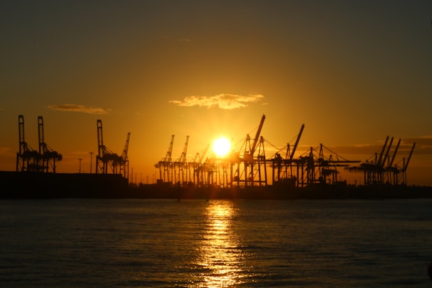 Sunset view over the port of Candeias with silhouettes of ships and cranes.