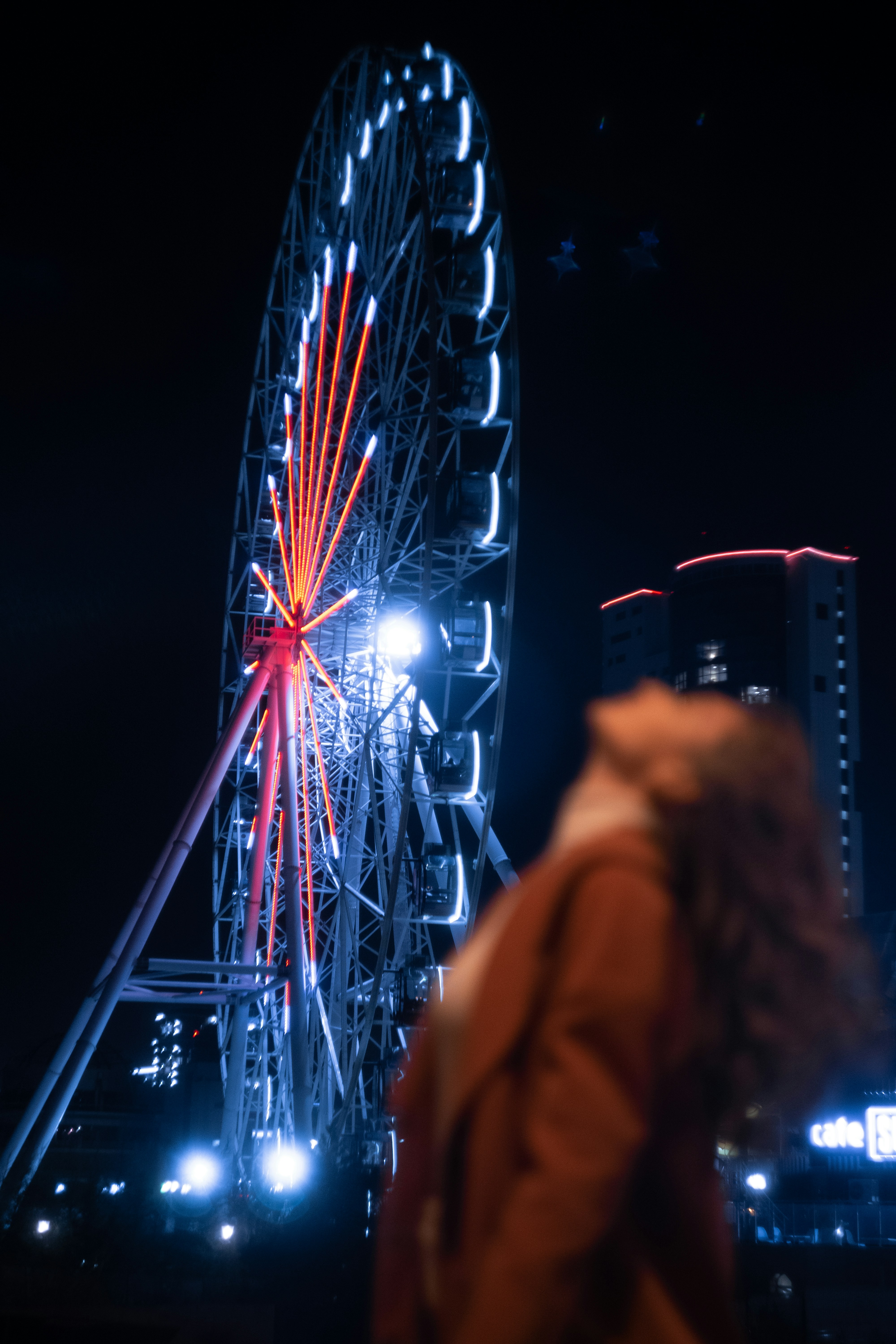 Femme en veste jaune debout près de la grande roue pendant la nuit