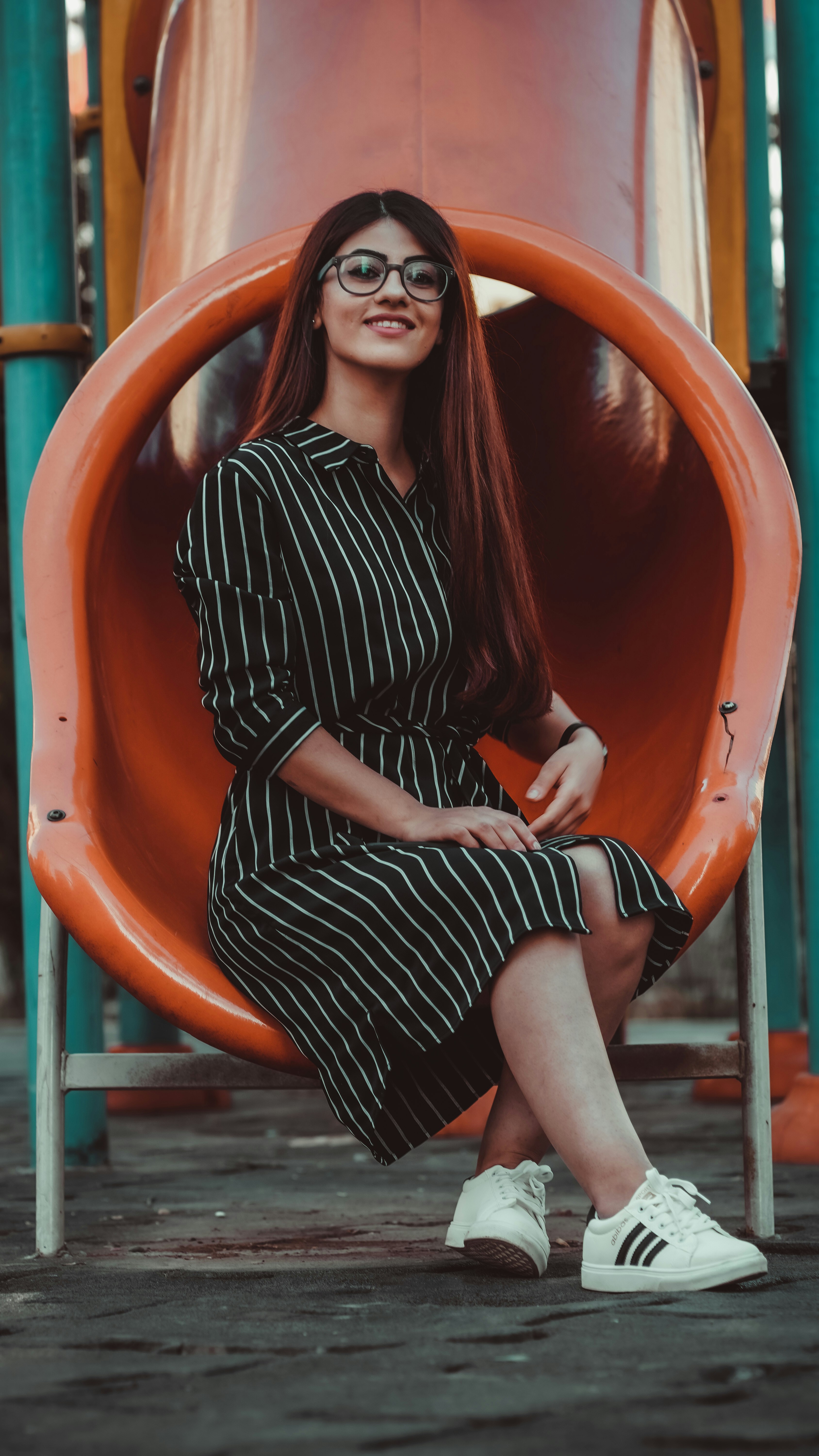 Wanita dengan gaun lengan panjang garis hitam dan putih duduk di slide oranye