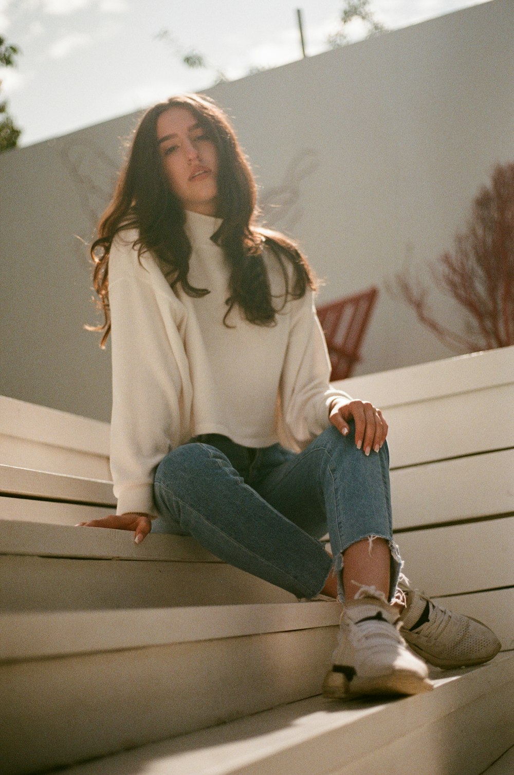 woman in white sweater and blue denim jeans sitting on white wooden bench