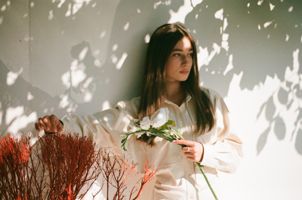 a woman standing next to a wall holding a bouquet of flowers