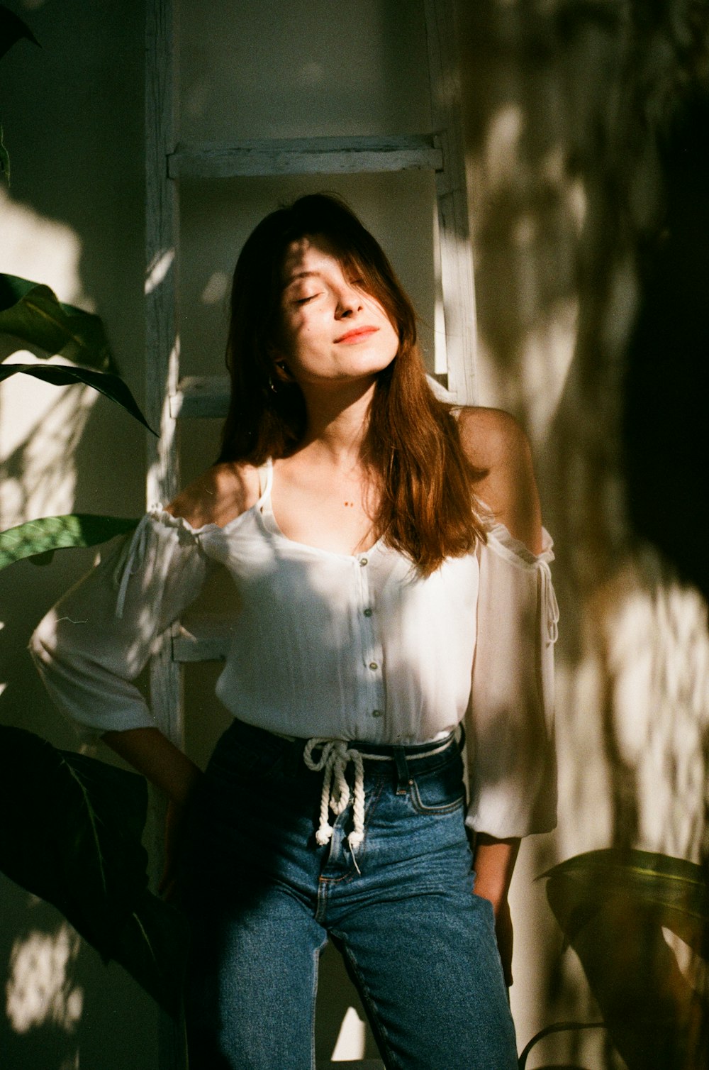 woman in white tank top and blue denim bottoms standing near green leaf plant