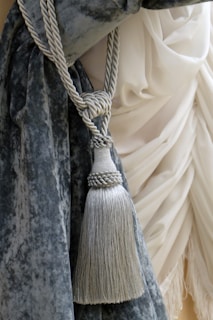 A luxurious blue velvet curtain is elegantly tied back with a decorative silver tassel rope, set against billowing white fabric in the background.
