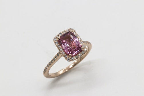 A gold ring featuring a large rectangular pink gemstone in the center, surrounded by a halo of small diamonds set on the band.