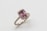 A gold ring featuring a large rectangular pink gemstone in the center, surrounded by a halo of small diamonds set on the band.