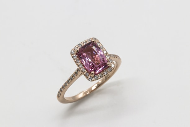 A gold ring featuring a large rectangular pink gemstone in the center, surrounded by a halo of small diamonds set on the band.