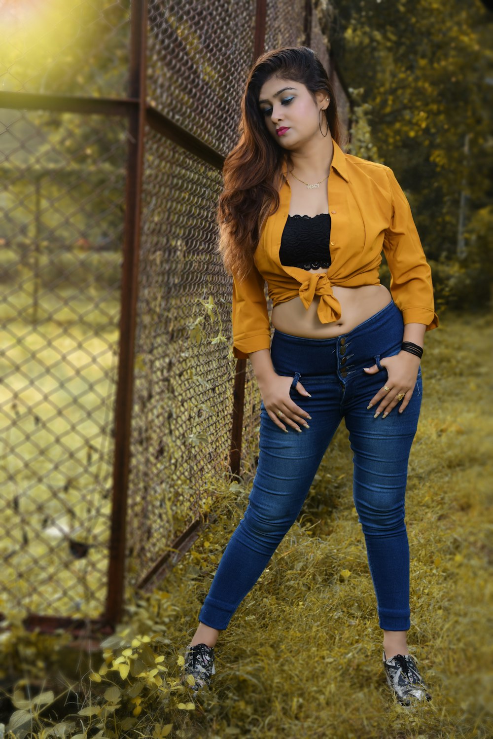 woman in yellow jacket and blue denim jeans leaning on chain link fence
