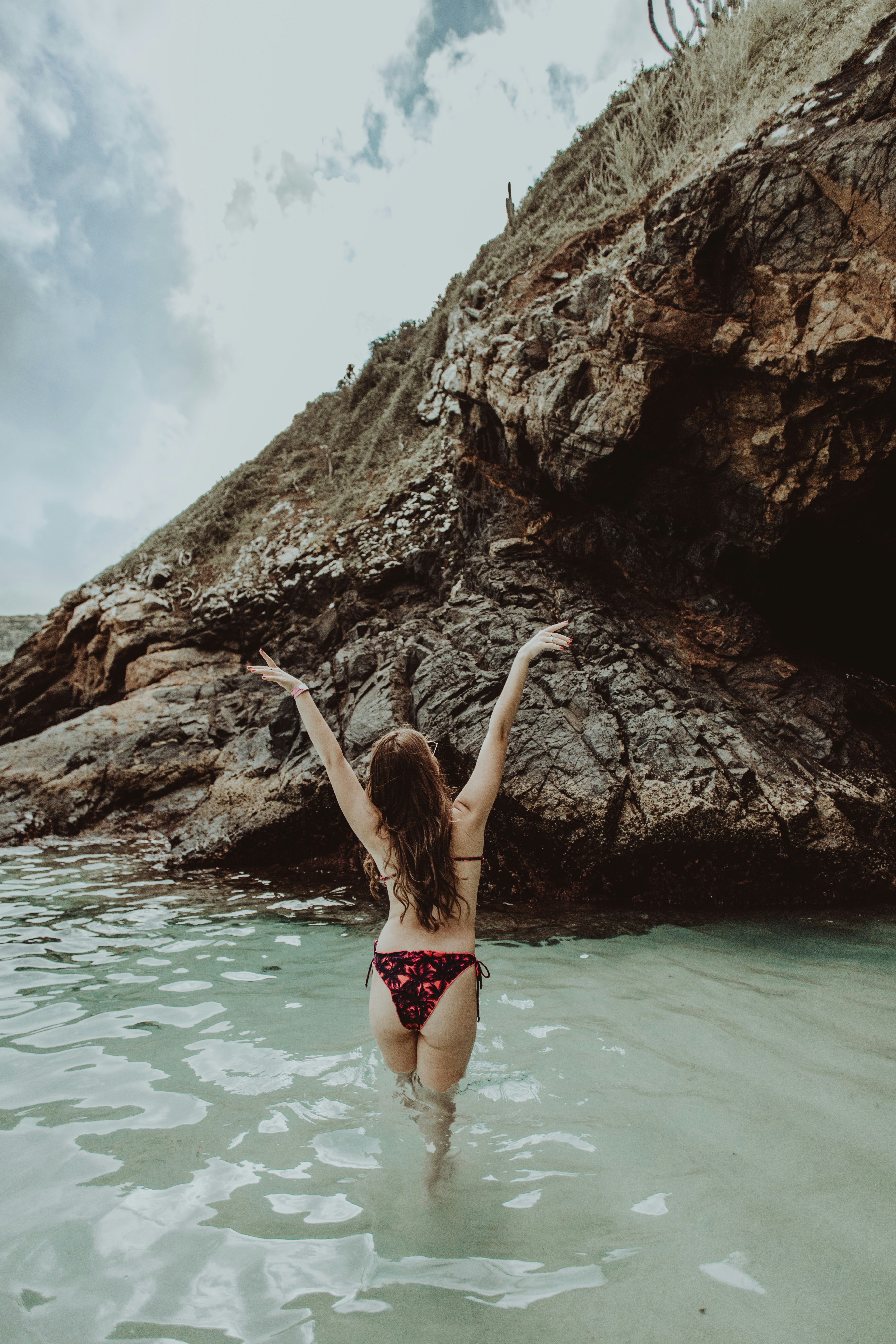 woman in pink and white bikini lying on rock near body of water during daytime