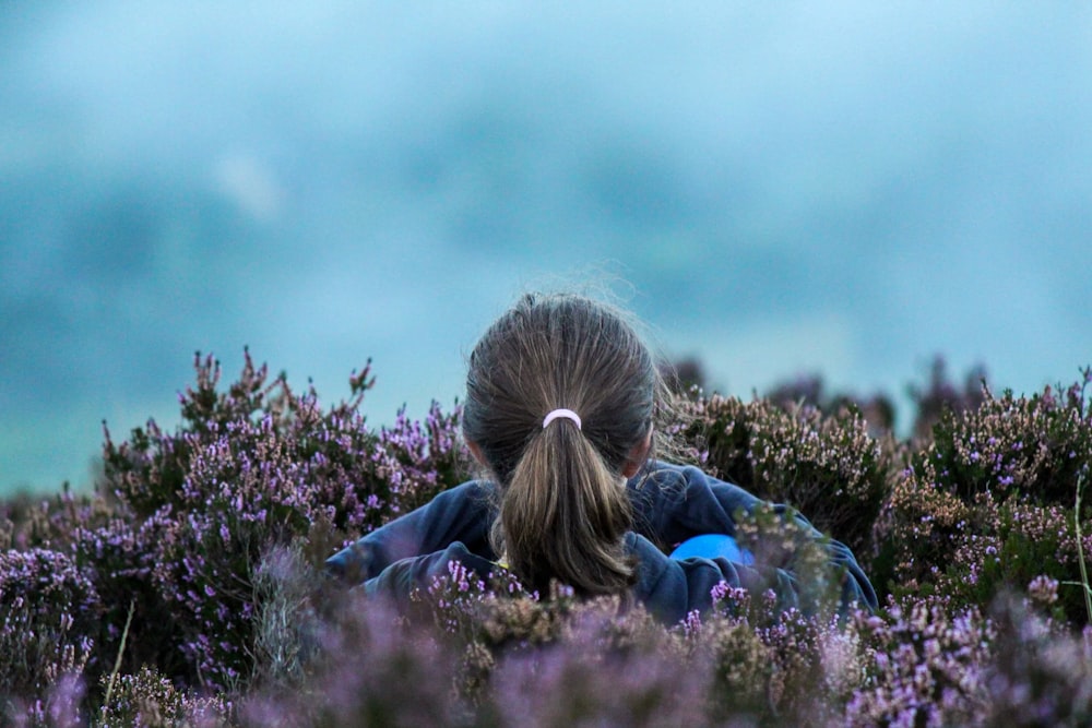 woman in blue jacket sitting on purple flower field during daytime