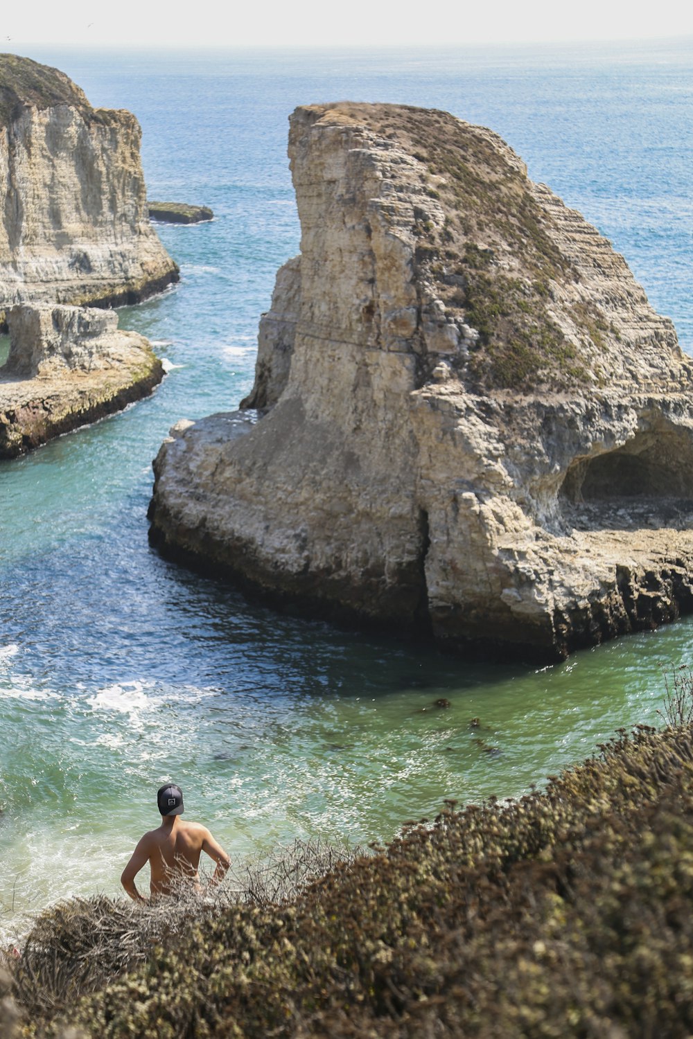 man in black shorts sitting on rock formation in front of body of water during daytime