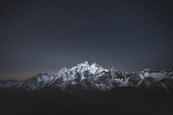 Snow-capped mountain peaks shimmering against a deep midnight black sky.