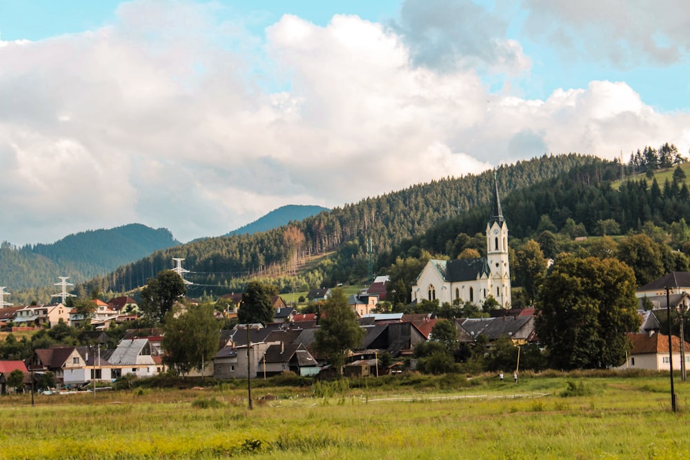 weißes und braunes Haus in der Nähe von grünen Bäumen und Bergen unter weißen Wolken und blauem Himmel während