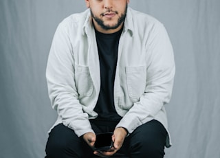 man in white dress shirt and black pants sitting on white floor