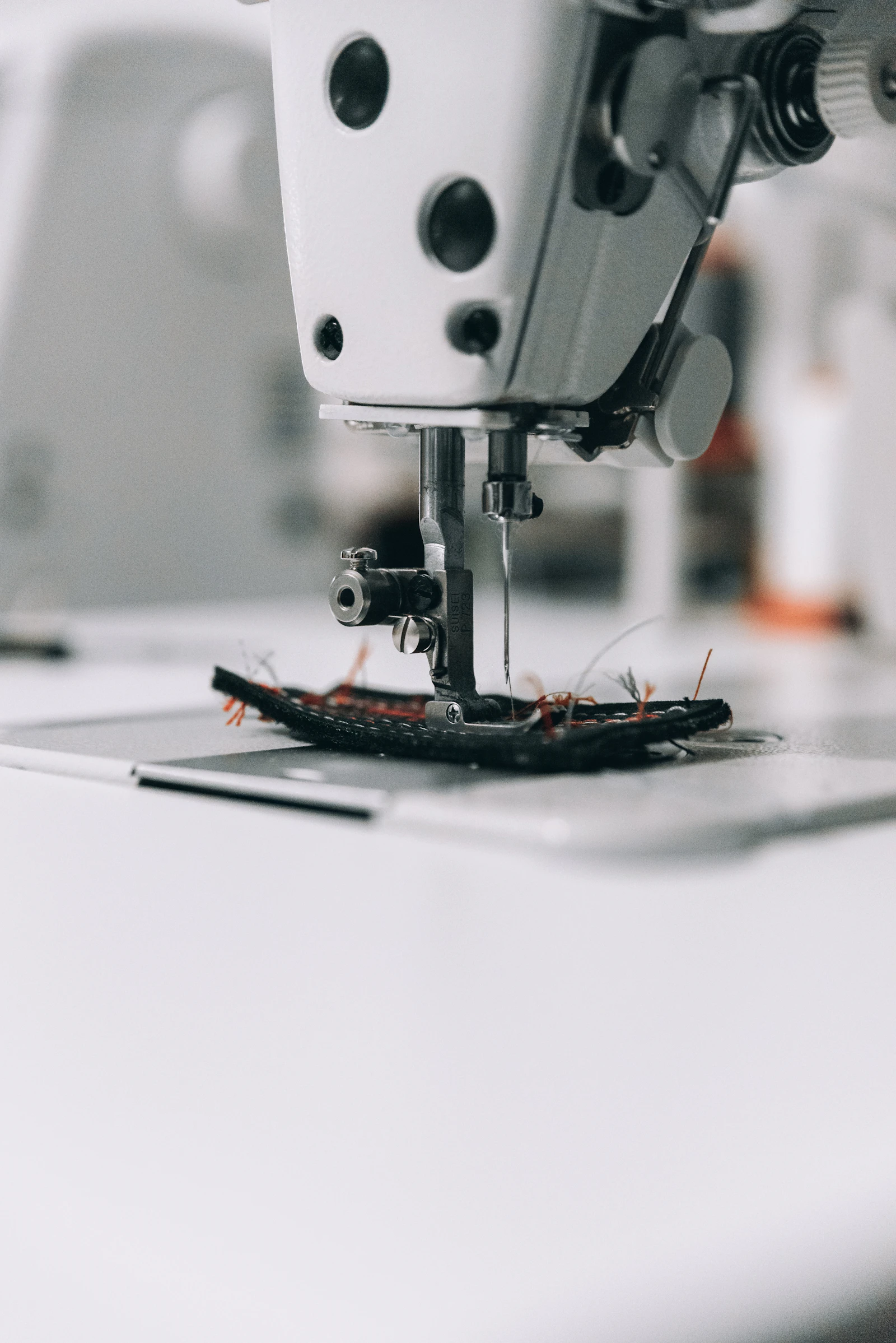 Heavy-duty industrial sewing machine stitching thick black webbing and heavy fabric with contrasting thread on a factory workbench