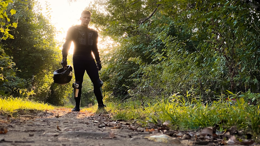 man in black pants carrying black backpack walking on dirt road during daytime