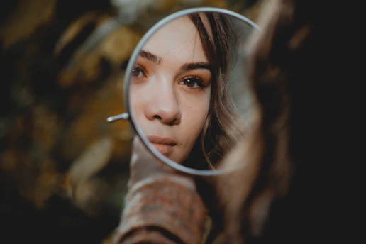 A woman looking at her reflection in a small round handheld mirror