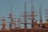Workers are standing on steel scaffolding at a construction site, engaged in various tasks. The structure consists of wooden planks and metal rods reaching upward against a clear blue sky.