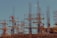 Workers are standing on steel scaffolding at a construction site, engaged in various tasks. The structure consists of wooden planks and metal rods reaching upward against a clear blue sky.