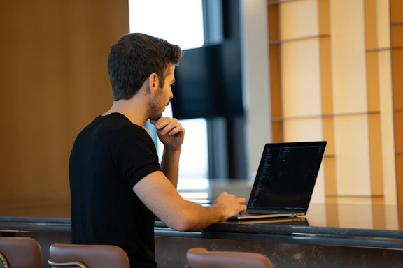 A focused male student working intently on a laptop in a minimal, modern study space.