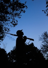 A hunter examining a well-maintained rifle outdoors at dawn.