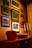 A wall adorned with multiple framed vintage photographs arranged in a gallery style, surrounded by a warm, ambient light. Below the frames is a wooden cabinet topped with decorative items including a red bucket and candlesticks.