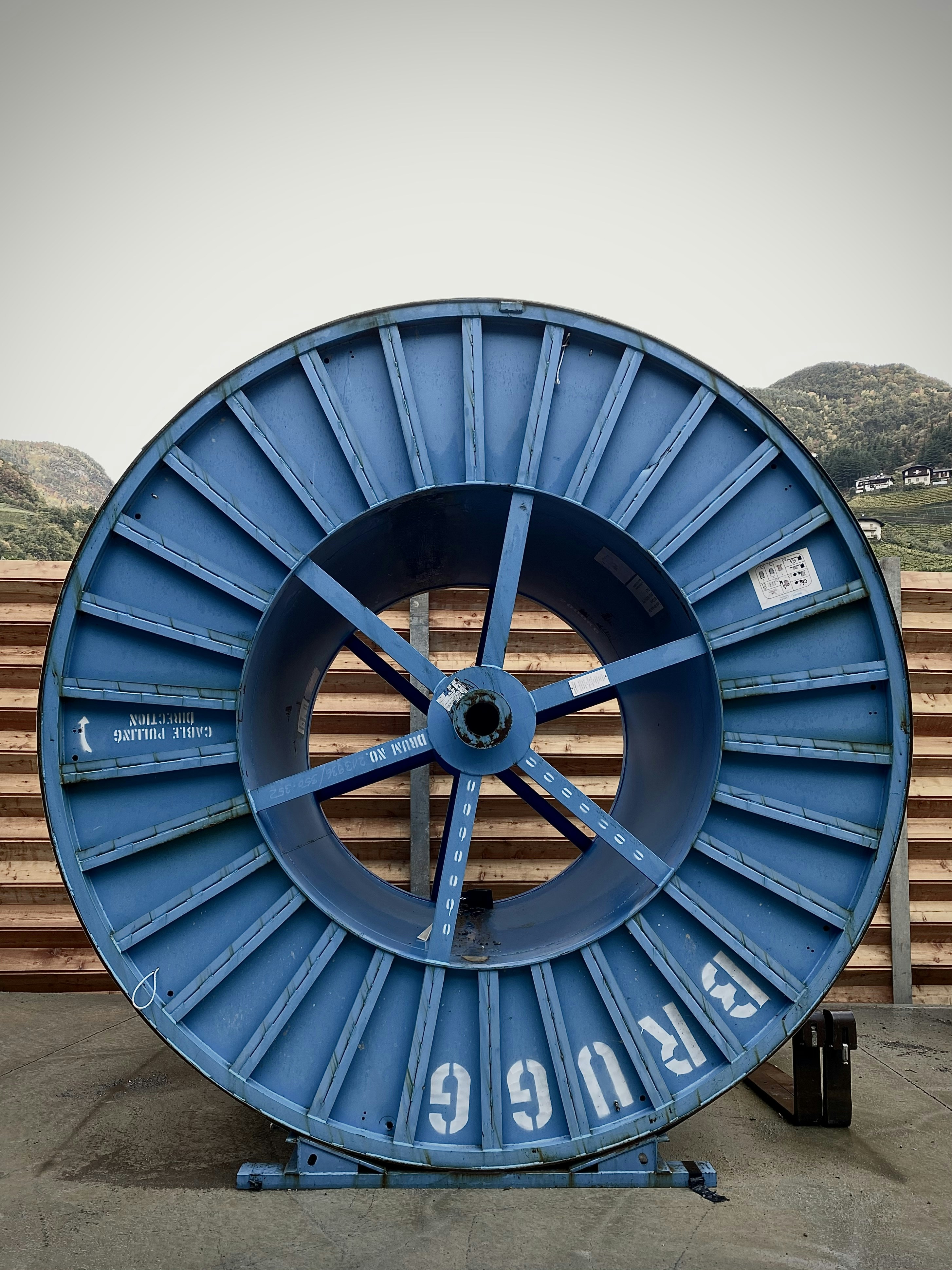 Weathered blue industrial cable spool stands on a concrete surface.
