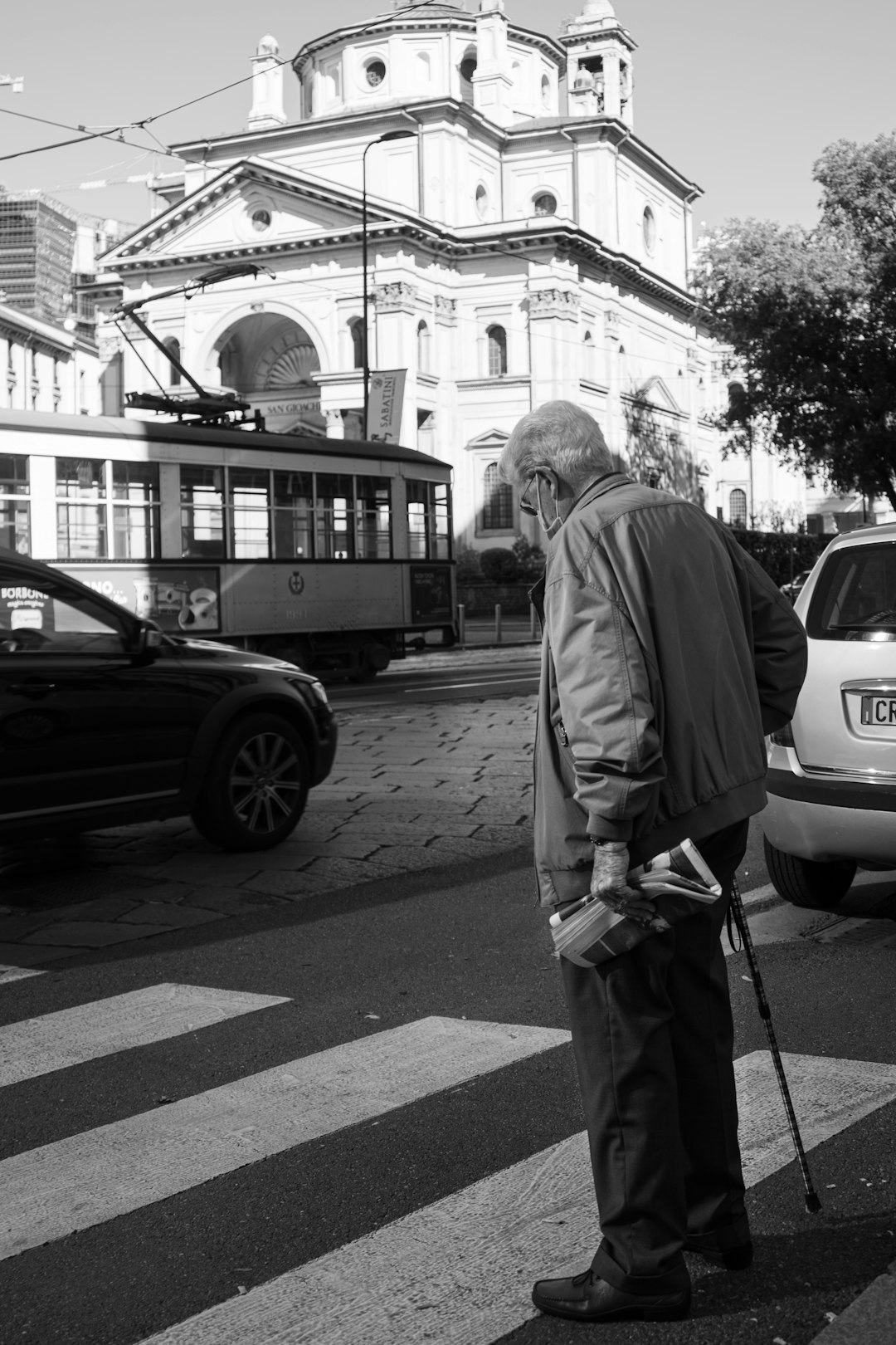 grayscale photo of woman in coat standing on sidewalk