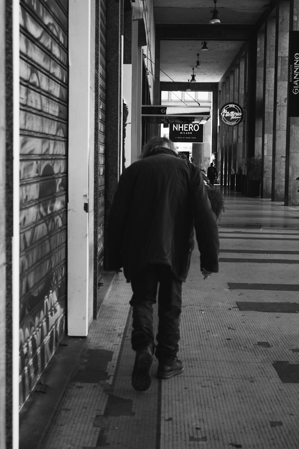 man in black coat walking on sidewalk in grayscale photography